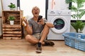 Young blond man doing laundry using smartphone crazy and mad shouting and yelling with aggressive expression and arms raised Royalty Free Stock Photo