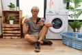 Young blond man doing laundry using smartphone pointing down looking sad and upset, indicating direction with fingers, unhappy and Royalty Free Stock Photo