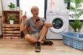 Young blond man doing laundry using smartphone pointing finger up with successful idea Royalty Free Stock Photo