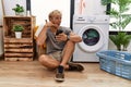 Young blond man doing laundry using smartphone smiling doing phone gesture with hand and fingers like talking on the telephone Royalty Free Stock Photo