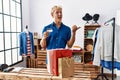 Young blond man holding credit card working as manager at retail boutique pointing thumb up to the side smiling happy with open Royalty Free Stock Photo