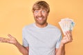 Young blond man holding united kingdom pounds celebrating achievement with happy smile and winner expression with raised hand