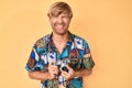 Young blond man holding vintage camera smiling and laughing hard out loud because funny crazy joke Royalty Free Stock Photo