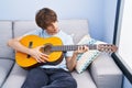 Young blond man playing classical guitar sitting on sofa at home Royalty Free Stock Photo