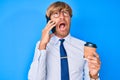 Young blond man talking on the smartphone and drinking a cup of coffee angry and mad screaming frustrated and furious, shouting Royalty Free Stock Photo