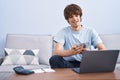 Young blond man using laptop holding dollars at home Royalty Free Stock Photo