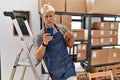 Young blond man using smartphone working at storehouse pointing down looking sad and upset, indicating direction with fingers, Royalty Free Stock Photo