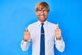 Young blond man wearing business clothes and glasses success sign doing positive gesture with hand, thumbs up smiling and happy Royalty Free Stock Photo