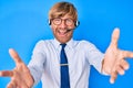 Young blond man wearing call center agent headset looking at the camera smiling with open arms for hug Royalty Free Stock Photo