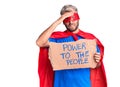 Young blond man wearing super hero custome holding power to the people cardboard banner stressed and frustrated with hand on head,