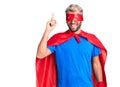 Young blond man wearing super hero custome pointing finger up with successful idea
