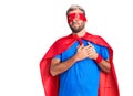 Young blond man wearing super hero custome smiling with hands on chest with closed eyes and grateful gesture on face Royalty Free Stock Photo