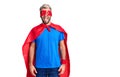 Young blond man wearing super hero custome sticking tongue out happy with funny expression