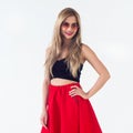 Young blond model presenting new fashionable summer look, wearing circle sunglasses, red skirt and black sleeveless top Royalty Free Stock Photo