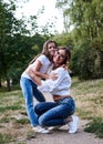 Young blond mother hugging her brunette daughter in the park in summer. Woman and girl, wearing blue jeans and white t-shirts, Royalty Free Stock Photo