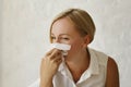 Young blond pretty sick with flu businesswoman sitting at her working place holding white napkins. Sick freelancer concept.