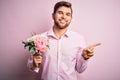 Young blond romantic man with beard and blue eyes holding beautiful bouquet of flowers very happy pointing with hand and finger to Royalty Free Stock Photo