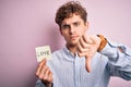 Young blond romantic man with curly hair holdiing paper with love message for valentines day with angry face, negative sign