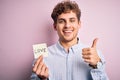 Young blond romantic man with curly hair holdiing paper with love message for valentines day happy with big smile doing ok sign,