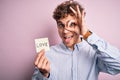 Young blond romantic man with curly hair holdiing paper with love message for valentines day with happy face smiling doing ok sign