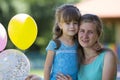 Young blond smiling happily mother hugs lovingly and protectively her small pretty preschool daughter girl with bright balloons on