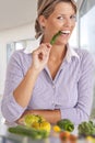 Young blond smiling woman eating green chili pepper standing in front of a table full of vegetable on a kitchen Royalty Free Stock Photo