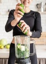 Young blond smiling woman making cucumber smoothie at home kitchen