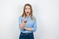 Young blond surprised woman looks curious pointing with her hand standing on isolated white background