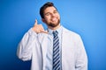 Young blond therapist man with beard and blue eyes wearing coat and tie over background smiling doing phone gesture with hand and Royalty Free Stock Photo