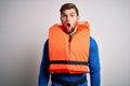 Young blond tourist man with beard and blue eyes wearing lifejacket over white background afraid and shocked with surprise Royalty Free Stock Photo