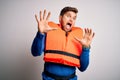 Young blond tourist man with beard and blue eyes wearing lifejacket over white background afraid and terrified with fear