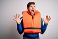 Young blond tourist man with beard and blue eyes wearing lifejacket over white background crazy and mad shouting and yelling with Royalty Free Stock Photo