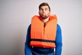 Young blond tourist man with beard and blue eyes wearing lifejacket over white background making fish face with lips, crazy and Royalty Free Stock Photo