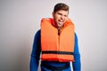 Young blond tourist man with beard and blue eyes wearing lifejacket over white background winking looking at the camera with sexy Royalty Free Stock Photo