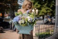 Young blond woman with beautiful basket with different fresh flowers in her hands