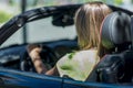 Young blond woman driving a cabriolet car stopped at a light.