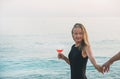 Young blond woman holding glass of rose wine and man's hand on beach by the sea at sunset. Alanya, Turkey. Royalty Free Stock Photo