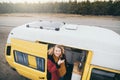 Young blond woman looking out of camper van with solar panel on the roof top and pine forest on the background Royalty Free Stock Photo