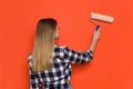 Young Woman Painting Orange Wall. Rear View