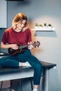 Young blond woman playing ukulele at home on table Royalty Free Stock Photo