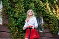 Young blond woman, posing with black electric scooter in city center old historical building covered with green plants. Summer Royalty Free Stock Photo