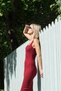 Young blond woman in a red dress leaning against the wooden fence. Royalty Free Stock Photo