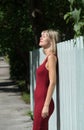Young blond woman in a red dress leaning against the wooden fence. Royalty Free Stock Photo