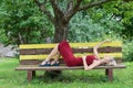 Young blond woman in a red dress leaning sits on a wooden bench. Royalty Free Stock Photo