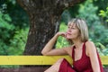 Young blond woman in a red dress leaning sits on a wooden bench. Royalty Free Stock Photo