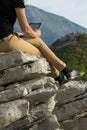 Young blond woman sitting on the edge of the mountain cliff using digital tablet Royalty Free Stock Photo