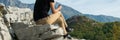 Young blond woman sitting on the edge of the mountain cliff using the smartphone. Technology outdoors lifestyle/travel t Royalty Free Stock Photo