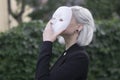 Young blond woman taking off a mask. Pretending to be someone else concept. outdoors.