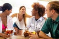 Young blond woman talking to friends in beach bar while having drinks together. Multiracial friends having fun. Royalty Free Stock Photo