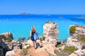 Young woman on the top of the rock cliff looks at paradise clear torquoise blue water with boats and cloudy blue sky in background Royalty Free Stock Photo